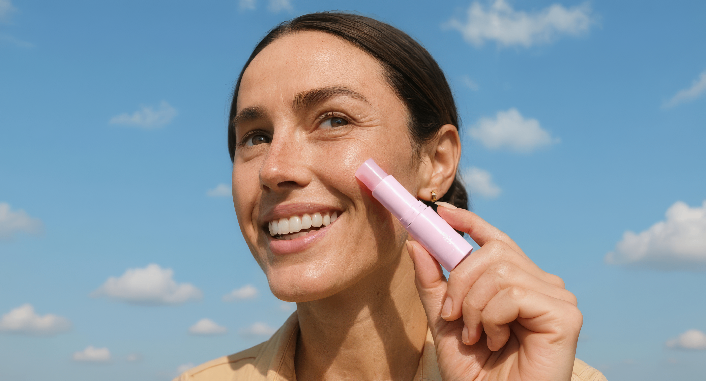 Woman applying sunscreen with a stick against a blue sky
