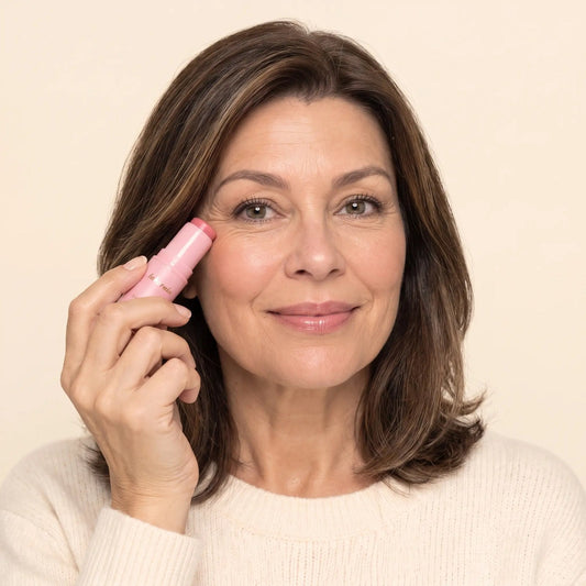 A woman gliding the pink Cleo balm stick over the fine lines at the corner of her eye