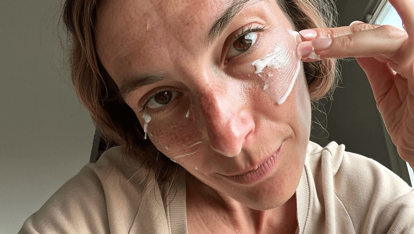 Woman applying cream to her face with a neutral background